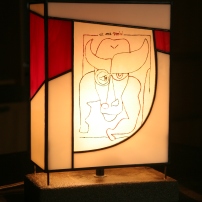 Lampe Tiffany reproduisant le dessin "et me voici" de Claude Nougaro montée sur socle béton. Avec l'aimable autorisation de Mme Hélène Nougaro